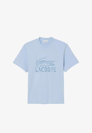 Camiseta de manga corta azul claro con logo de cocodrilo bordado y texto "LACOSTE" centrados en el pecho.