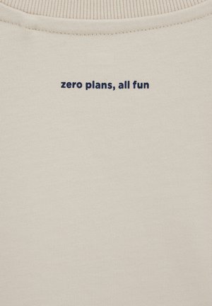 Beżowa tkanina z granatowym napisem umieszczonym centralnie przy dekolcie: "zero planów, cała zabawa" na ubraniu z prążkowanym kołnierzem.