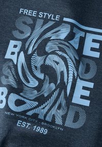 Tmavošedé tričko s modrým grafickým textom a víriacimi vzormi, na ktorom je napísané "FREE STYLE SKATEBOARD" a v spodnej časti "EST. 1989".