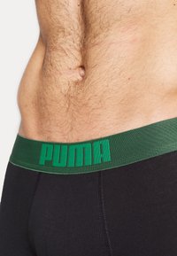 Zwarte boxershorts met een groene elastische tailleband, voorzien van het "PUMA"-logo in vetgedrukte letters. De stof lijkt glad en heeft een aansluitende pasvorm.