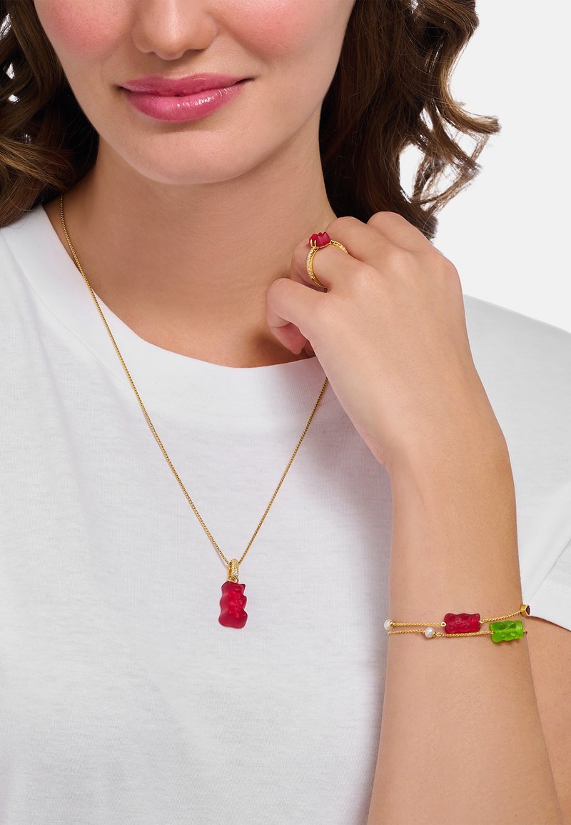 Goldene Halskette mit einem roten Gummibär-Anhänger, kombiniert mit einem Ring mit einem roten Gummibär und einem Armband mit roten und grünen Gummibären.