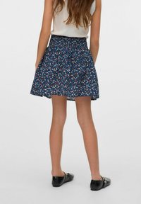Falda de estampado floral en azul oscuro, con cintura elástica y diseño acampanado. Combinada con zapatos de tacón bajo en negro.