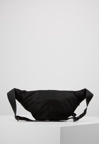 Bolsa de cintura de tela negra con una textura suave, correa ajustable, cierre de cremallera y un diseño minimalist. Apta para uso casual.