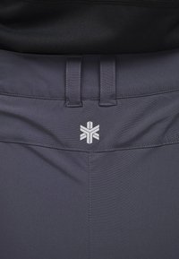 Donkergrijze sportshorts met een gladde stof, een platte tailleband met lussen en een wit logo gecentreerd op de achterkant.