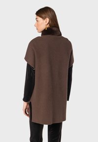 Poncho en laine marron avec un col en fausse fourrure, manches courtes, fentes sur les côtés et coupe décontractée. Tissu texturé avec des détails lisses.