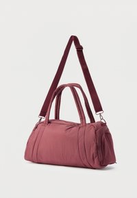 Μπορντό μαλακή τσάντα duffel με διπλές λαβές και ρυθμιζόμενο ιμάντα ώμου, εμφανίζεται σε κεκλιμένη γωνία σε απλό λευκό φόντο.