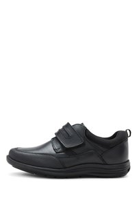 Chaussure en cuir noir avec une finition lisse, dotée de deux bandes Velcro et d'un capuchon de pied texturé. La semelle est robuste et présente une légère courbure.
