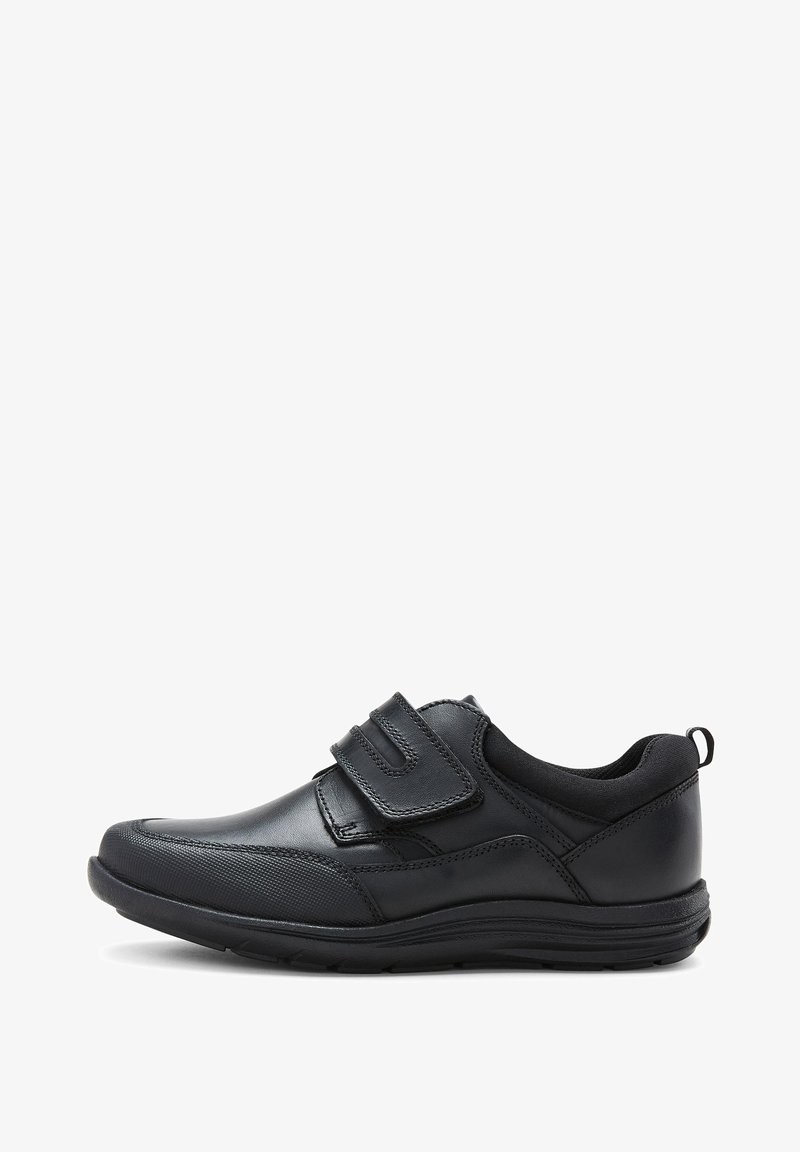 Chaussure en cuir noir avec une finition lisse, dotée de deux bandes Velcro et d'un capuchon de pied texturé. La semelle est robuste et présente une légère courbure.