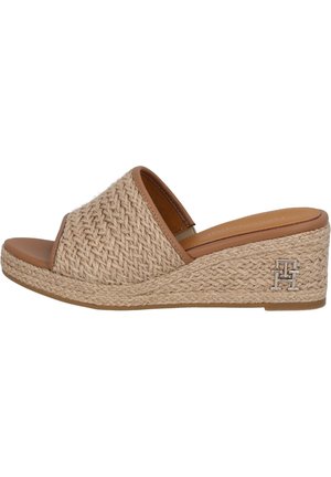 Beżowa sandałka na koturnie z plecioną fakturą, otwartym palcem, stylem typu slip-on i małym srebrnym logo na boku pięty.