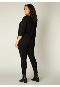 Zwarte casual top met driekwartmouwen, ontspannen pasvorm, gecombineerd met zwarte skinny jeans en enkellaarsjes. Glad materiaal, minimalistisch design.