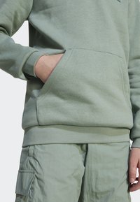 Sweatshirt verde claro com bolso canguru, punhos e bainha canelados. Combinado com calças cargo verde claro. Textura suave.