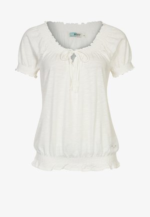 Blouse blanche à manches courtes avec encolure froncée, détail à nouer, ourlets élastiques et petit logo en forme de cœur près du bas.