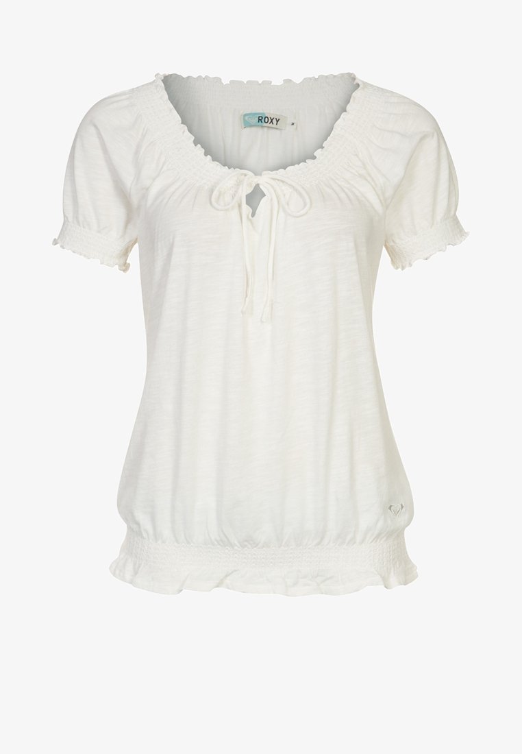 Blouse blanche à manches courtes avec encolure froncée, détail à nouer, ourlets élastiques et petit logo en forme de cœur près du bas.