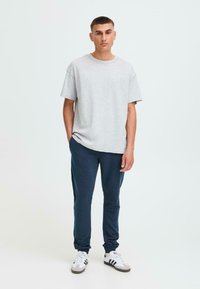 Grijze katoenen T-shirt met een losse pasvorm, gecombineerd met donkerblauwe joggingsbroeken. Sneakers hebben witte en zwarte strepen. Eenvoudig, comfortabel ontwerp.