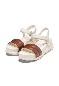 Sandalias de plataforma con una tira frontal de cuero marrón, una tira de tobillo ajustable blanca y una suela texturizada en crema. Diseño voluminoso con punta redonda.
