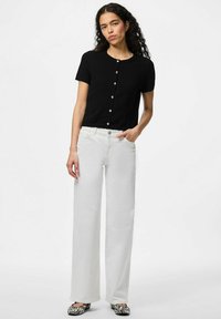 Musta lyhythihainen neuletakki, jossa on sydämenmuotoiset napit, yhdistettynä valkoisiin leveälahkeisiin farkkuihin ja musta-valkoisesti kuvioituihin kenkiin.