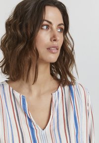 Juostuota bliuska su vertikaliais raštais mėlyna, raudona ir juoda spalvomis ant šviesaus fono. Lengvas audinys su V formos iškirpte.