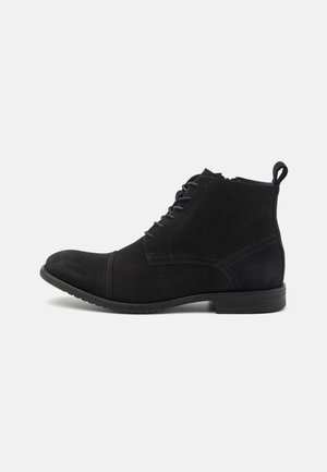 Bottines en daim noir avec bout arrondi, lacets à l'avant et languette à l'arrière. La semelle est texturée pour une meilleure adhérence.