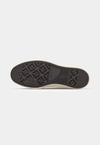 Svart gummisåle med diamant- og heksagonale mønstre, beige kanter, og logoen "Converse All Star" synlig.