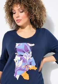 Dunkelblaues langärmliges Oberteil mit buntem floralem Grafikdesign in Lila und Orange, weiter Ausschnitt und weichem Stoff.