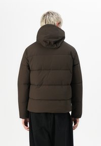 Brun dunjakke med hætte, quiltet design og elastiske manchetter. Glat tekstur, cropped snit og minimalistisch silhuet.
