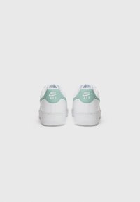 Bijele Nike Air tenisice s mint zelenim akcentom na peti. Gornjište od glatke kože i teksturirani gumeni potplat. Jednostavan dizajn s vezicama.