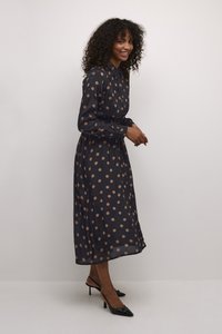 Langes navyblaues Kleid mit hellbraunen Punkten, Kragen, Knopfverschluss und Taillenzugdetail. Getragen mit schwarzen Absatzschuhen.