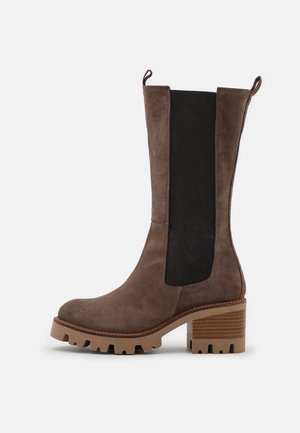Bottes cheville en daim marron avec panneaux latéraux élastiques noirs, talon en bois massif et semelle en caoutchouc texturée pour une meilleure adhérence et durabilité.