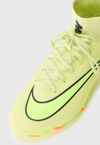 Scarpa da calcio gialla brillante realizzata in materiale texturizzato, con il logo Nike nero, lacci e dettagli arancioni sulla suola.
