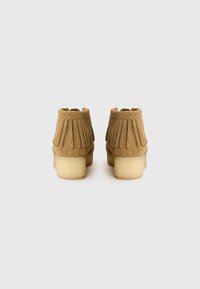 Bottines en suedine marron avec des détails frangés, bout rond et talon épais crème, mettant en valeur une texture douce et un design minimaliste.