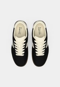 Μαύρα vegan αθλητικά παπούτσια με λευκές λεπτομέρειες και κορδόνια. Διαθέτουν υφή στην πάνω επιφάνεια και καφέ λαστιχένια σόλα. Στρογγυλεμένο σχήμα με χαμηλό προφίλ σχεδίαση.