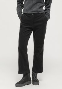 Svarta manchesterbyxor med platt front, raka ben, två sidofickor och knappstängning. Kombineras med svarta snörda plattformskängor.