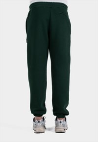 Donkergroene sweatpants met een elastische tailleband, zijzakken en afgewerkte enkels, gecombineerd met lichtgekleurde sportschoenen.