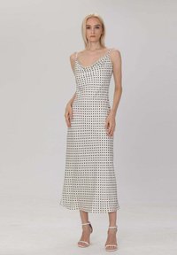 Robe midi à pois blancs avec un décolleté drapé, de fines bretelles, et une silhouette fluide, complétée par un tissu texturé.