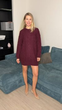 Noor naeratav noor naine, kandes burgundia värvi kootud kampsunist kleiti ja beeže kontsakingi, seisab elutoas sinise kordsidega diivani kõrval.