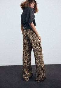 Pantalones de pierna ancha con estampado de leopardo, que presentan una paleta de colores en beige y marrón. Combinados con un top de punto oscuro, que resalta los materiales texturizados.