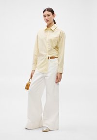 Dzeltena svītraina krekls ar apkakli, kopā ar plašām baltām biksēm. Brūns jostas siksna un neliela brūna soma papildina tērpu. Sudraba apavi.