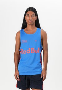 Modra mrežasta športna majica brez rokavov z rde�čimi poudarki in logotipom "Red Bull" v krepki pisavi. Ima krojen izrez in brezrokavno zasnovo. Uparjena z črnimi kratkimi hlačami.