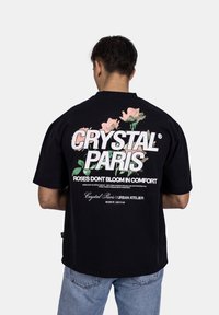 Černé oversized tričko s květinovou grafikou a výrazným textem na zadní straně. Vyrobené z bavlny, má krátké rukávy a volný střih.