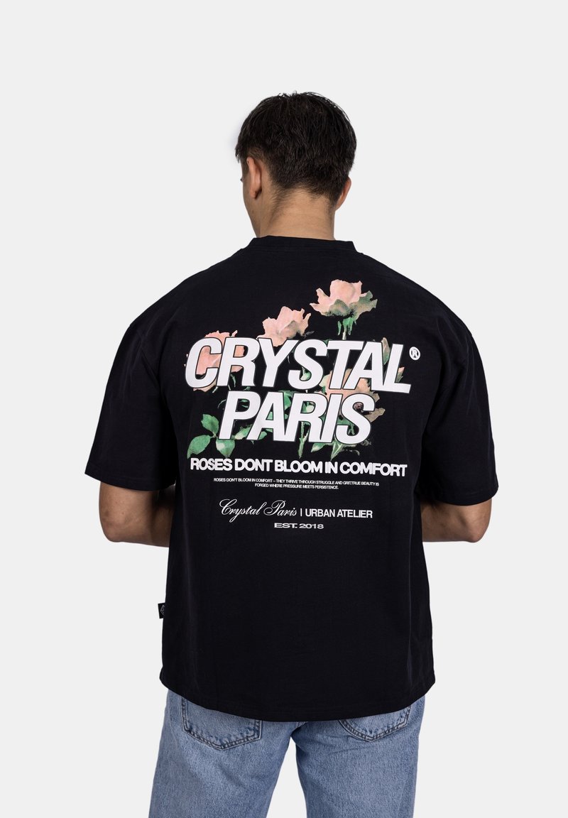 Černé oversized tričko s květinovou grafikou a výrazným textem na zadní straně. Vyrobené z bavlny, má krátké rukávy a volný střih.