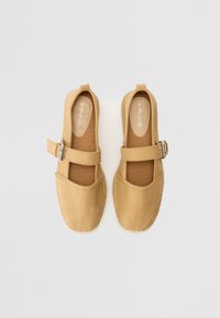 Espadrilles en suède beige avec un large orteil, une sangle à boucle réglable et des détails de semelle en jute tissé. Texture lisse avec des éléments de design minimaux.