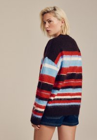 Multicolored striped sweater, featuring shades of red, blue, black, and white. Soft, fluffy texture with a ribbed hem and relaxed fit.