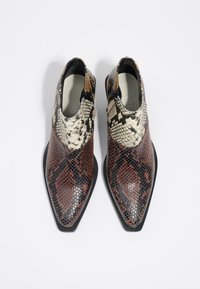 Botas de punta afilada con un patrón de piel de serpiente texturizado en marrón, negro y crema, con una suela negra elegante y un diseño de corte bajo.