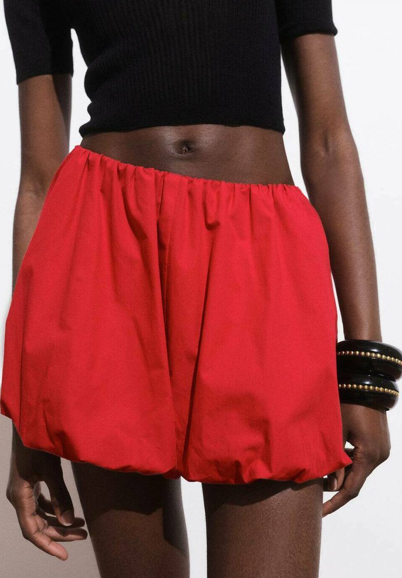 Rode, volumineuze shorts gemaakt van lichtgewicht stof met een elastische tailleband. Soepele textuur, verzameld ontwerp en knielange pasvorm. Zwarte armbandaccessoires.