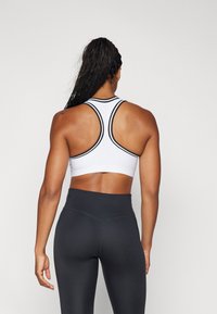 Hvit sports-BH med teksturert meshdesign og svart kant, parret med høyt midje svarte leggings, som viser racerback-kutt.