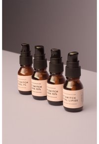 Vier bernsteinfarbene Glasflaschen mit schwarzen Pumpen, die rosa Etiketten tragen. Die Etiketten zeigen "Ret Switch" mit unterschiedlichen aktiven Inhaltsstoffen, darunter Retinol und AHA.