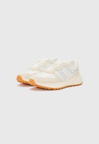Light beige running shoes with textured fabric, rubber soles, and a contrasting orange outsole. Features a side logo and cushioned tongue.