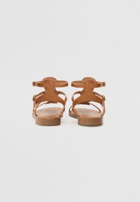 Sandales en cuir marron avec une semelle flatte, présentant plusieurs sangles et une boucle ajustable, à l'arrière ouvert, et texture lisse.