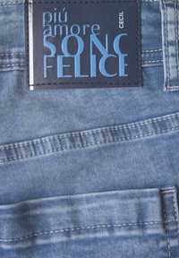 Tissu en denim bleu à délavage clair, avec une poche cousue et une étiquette en cuir rectangulaire avec du texte en relief en bleu clair et marine.
