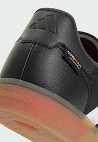 Black sneaker featuring durable textured materials, a translucent sole with a red tint, and a small "CORDURA" label on the side.